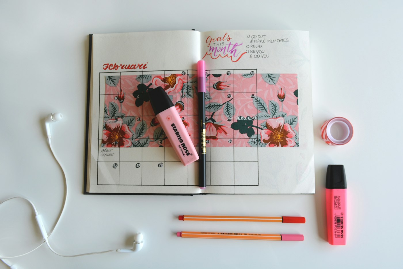 An open paper calendar with floral decoration, pencils and pink highlighters.
