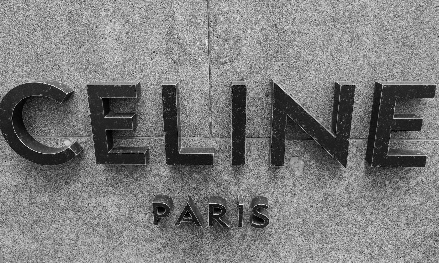 Dark metal Celine lettering against a textured pale stone wall.