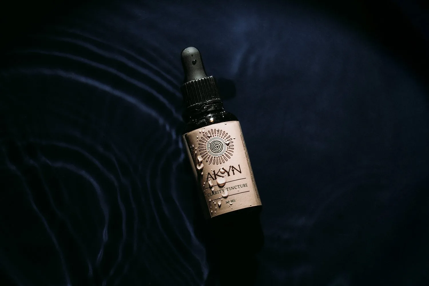 An AKYN dropper bottle on a dark rippled surface.