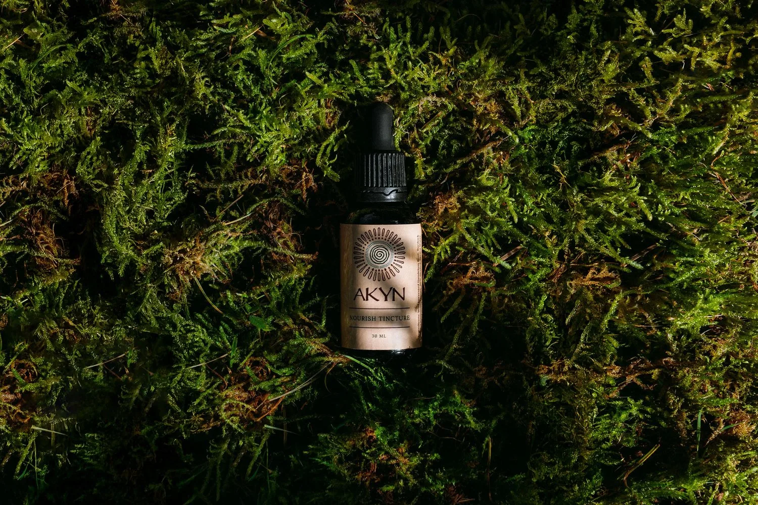 An AKYN bottle surrounded by green moss.
