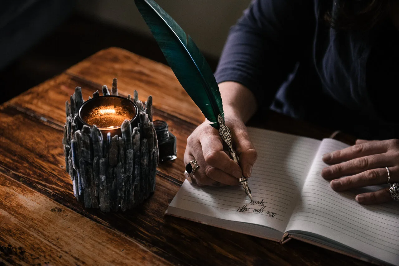 A hand writing beside a candle on timber.